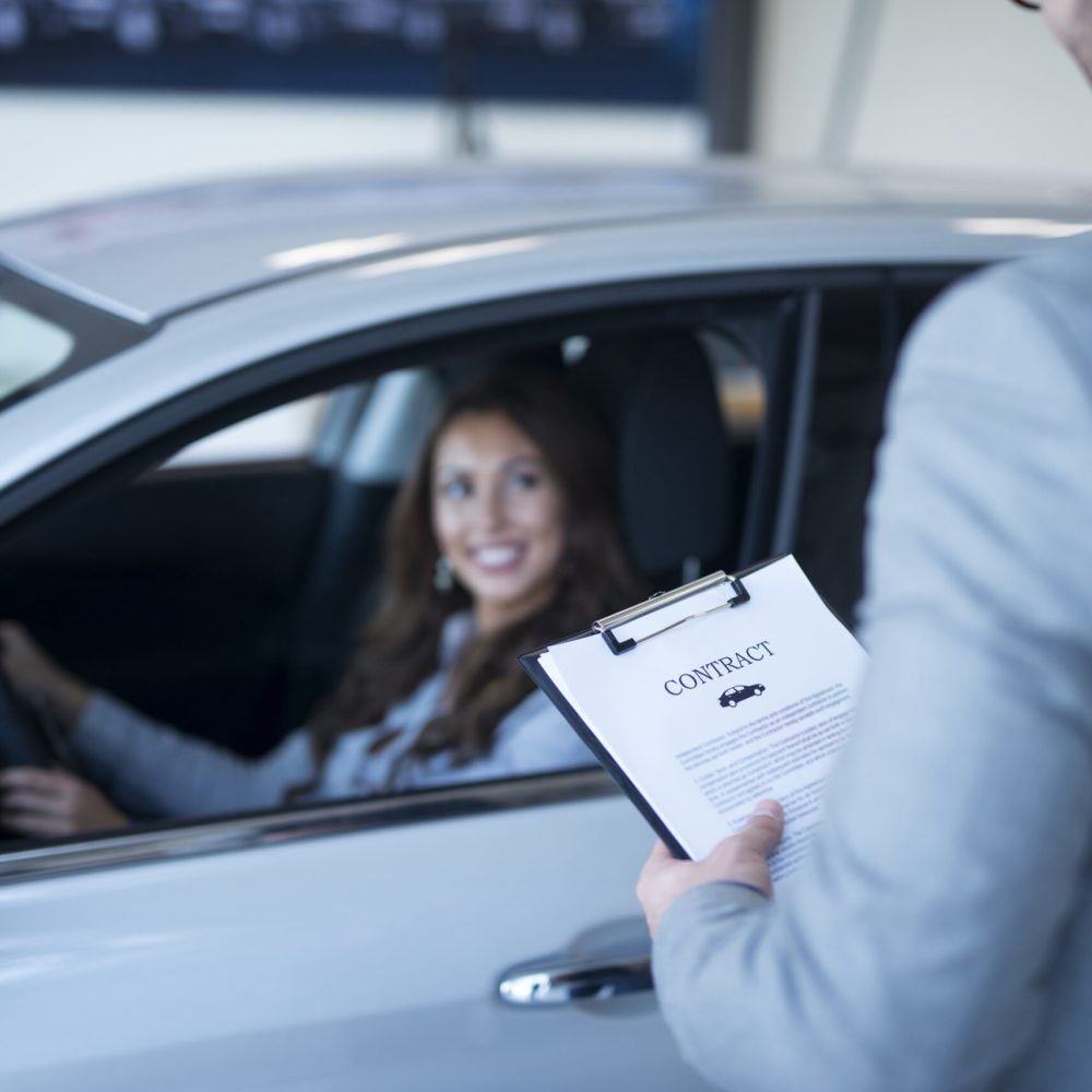 Happy customer buying new car at vehicle dealership.